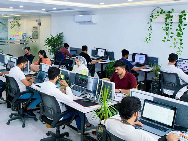 A team of custom software developers working in the ZAPTA office building in Lahore, Pakistan. The developers are working on a custom software development project, using various tools and technologies to create a high-quality software solution. The image is relevant to the keywords "about us," "custom software development company office," "web development company," "mobile app development company," "application development company," "IT consulting agency" "IT services company," "IT solutions company," "IT outsourcing company," "quality assurance," "mobile apps," "data analytics," "artificial intelligence," "machine learning," "MVP builder," "dedicated teams," "history of ZAPTA mission," and "ZAPTA office building."